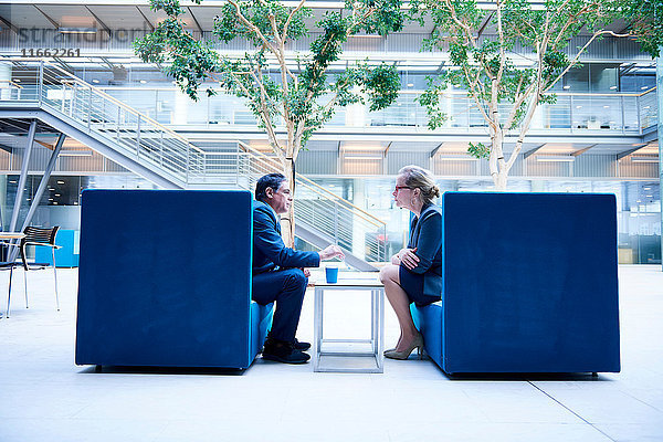 Geschäftsfrau und Mann bei Besprechung in Büro-Atrium-Sesseln