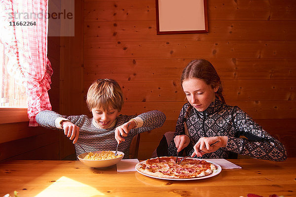 Teenager-Mädchen und Bruder essen Pasta und Pizza am Chalet-Tisch