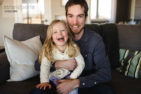 Porträt eines auf dem Sofa sitzenden Mannes mit Tochter auf dem Knie