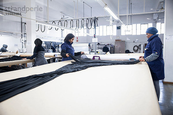 Fabrikarbeiter rollen Textilien auf Arbeitstisch in Bekleidungsfabrik aus