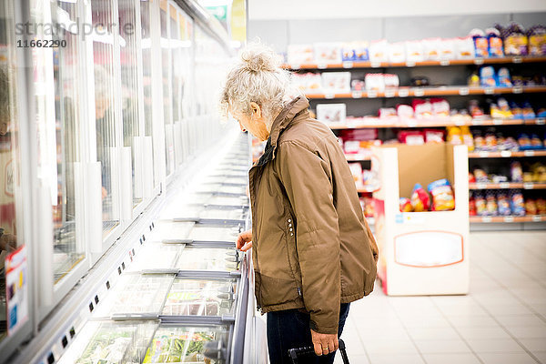 Reife Frau im Supermarkt  schaut in die Tiefkühltruhe