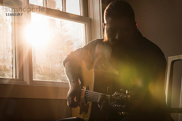 Mann spielt Gitarre neben dem Fenster