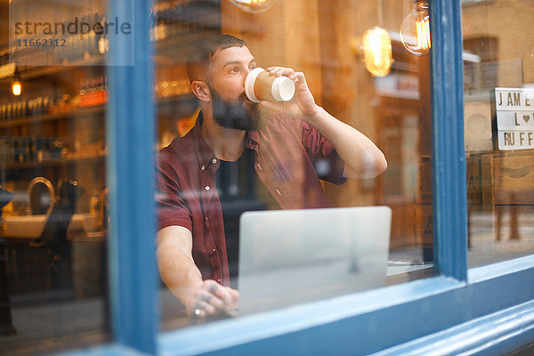 Fensteransicht des jungen Mannes beim Kaffeetrinken im Cafe