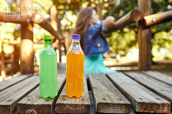 Teenager-Mädchen lehnt auf Klettergerüst im Park  im Vordergrund zwei Flaschen Erfrischungsgetränke