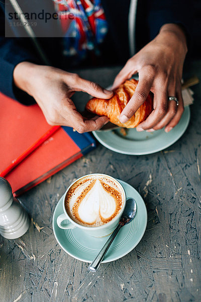 Draufsicht auf die Hand einer Frau  die im Cafe ein Croissant hält