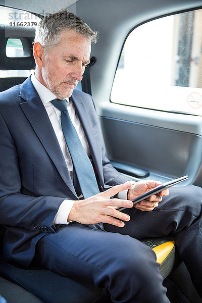 Der reife Geschäftsmann beim Betrachten des digitalen Tabletts im Taxi