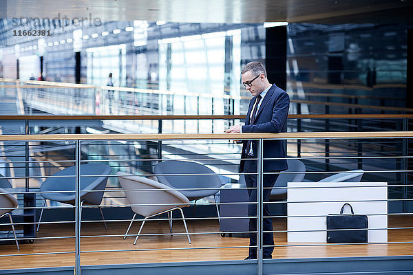 Geschäftsmann schaut auf Smartphone auf Bürobalkon