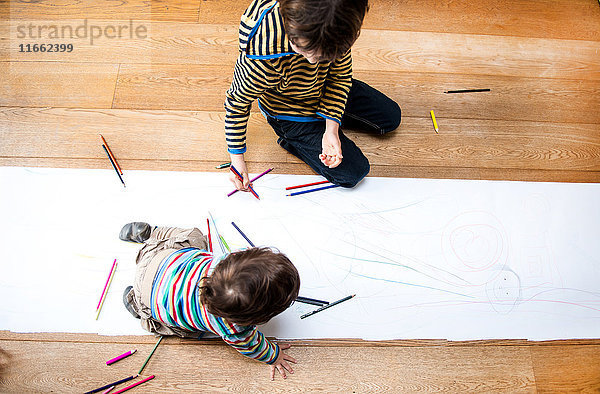 Draufsicht auf männliches Kleinkind und großen Bruder auf dem Boden sitzend - Zeichnung auf langem Papier