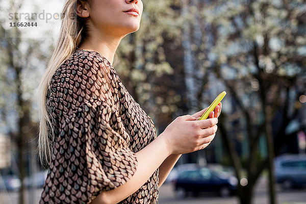 Schnappschuss einer jungen Frau mit Smartphone  die in der Stadt über die Schulter schaut.