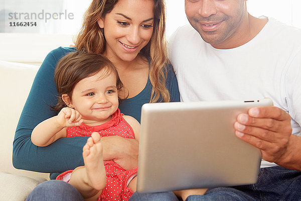Kleines Mädchen sitzt auf dem Sofa  die Eltern schauen auf das digitale Tablet