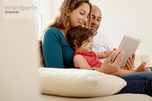 Kleines Mädchen sitzt auf dem Sofa  die Eltern schauen auf das digitale Tablet