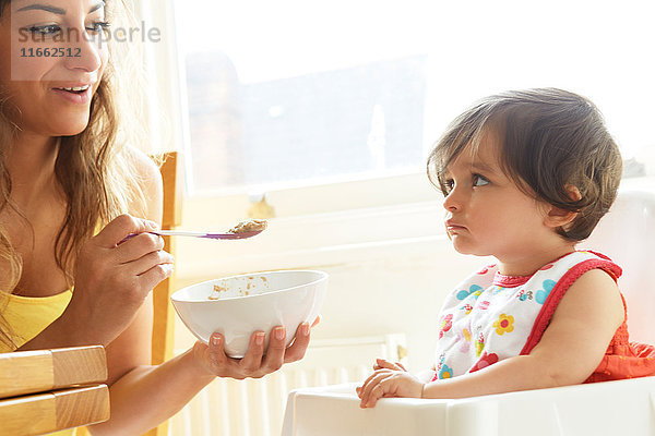 Frau füttert dickköpfiges Mädchen mit Frühstücksflocken