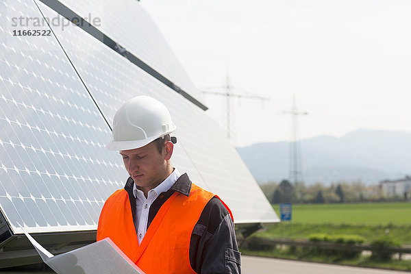 Männlicher Ingenieur schaut sich den Papierkram auf der Baustelle für Solarpaneele an