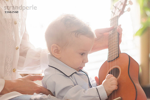 Mutter hält Gitarre und Baby spielt mit ihren Saiten