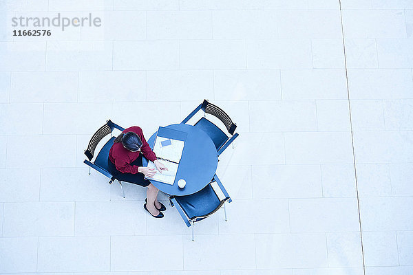 Draufsicht einer Geschäftsfrau  die am Tisch im Atrium des Büros Papierkram liest