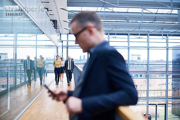 Geschäftsmann betrachtet Smartphone auf Bürobalkon