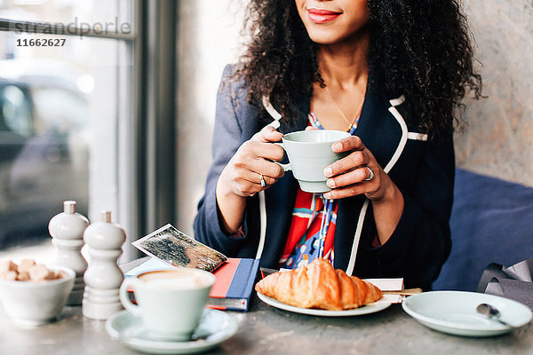 Ausschnitt einer Frau mit Kaffeetasse im Cafe