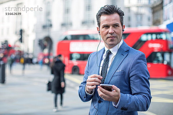 Geschäftsleute in der Straße mit Smartphone und Ohrhörern  London  UK