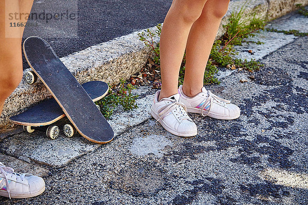 Zwei Freundinnen  im Freien stehend  Skateboards auf dem Boden neben ihnen  niedrige Sektion
