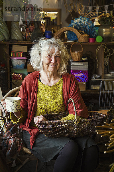 Frau sitzt in der Werkstatt einer Korbflechterin und hält einen Korb.
