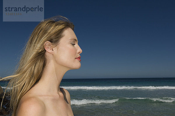 Frau mit langen blonden Haaren steht vor einem Ozean.