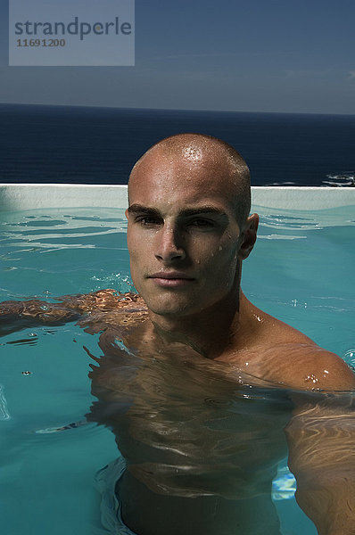 Kahlköpfiger junger Mann in einem Schwimmbad.