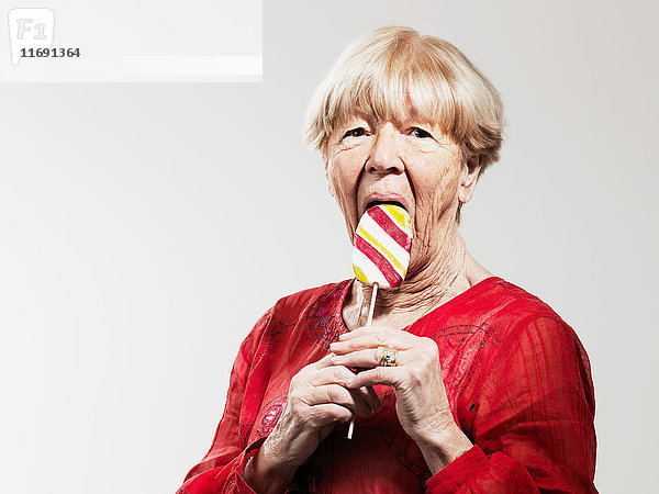 Ältere Frau isst Lolli vor weißem Hintergrund