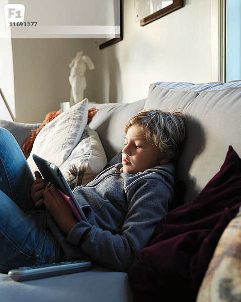 Teenager-Junge entspannt auf dem Sofa und mit digitalem Tablett