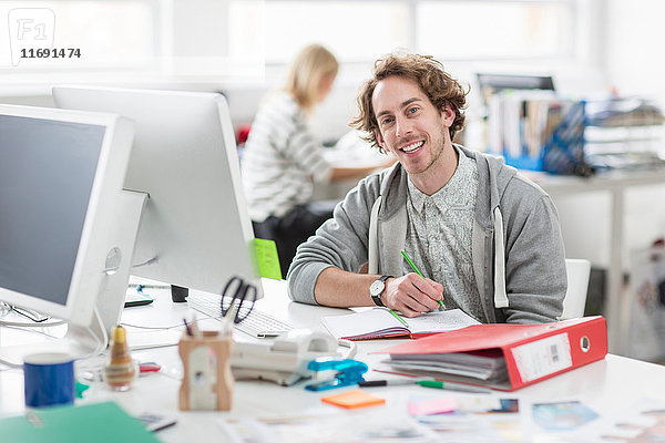 Junger Mann am Schreibtisch sitzend und lächelnd im Kreativbüro  Porträt