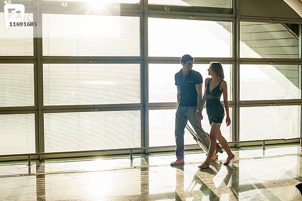 Junges Paar geht am Fenster im Sonnenlicht am Flughafen vorbei