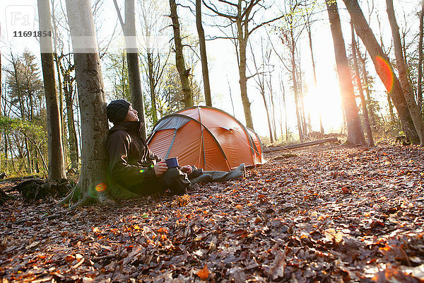 Mann trinkt Kaffee am Zelt im Wald