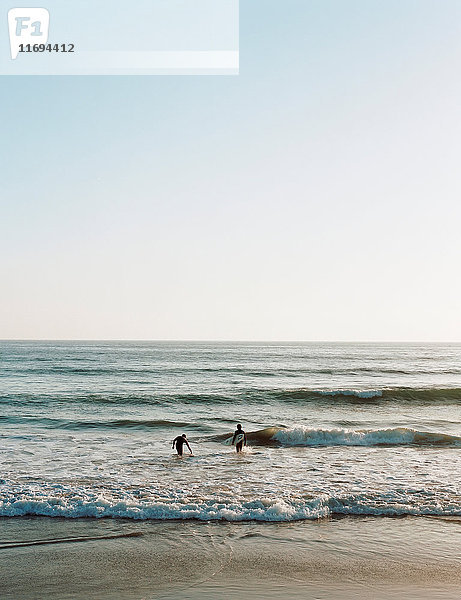 Surfer  die am Strand in Wellen laufen