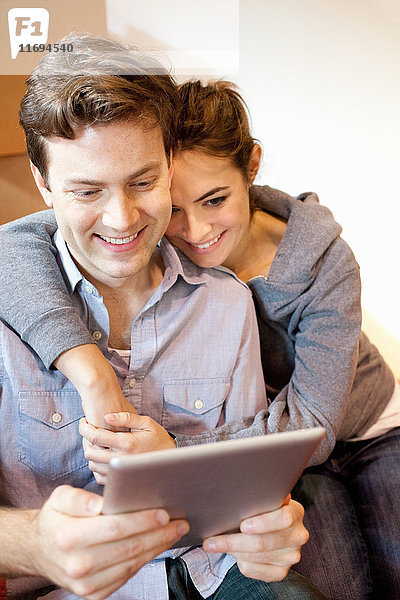 Junges Paar sitzt auf dem Boden und schaut auf ein digitales Tablett