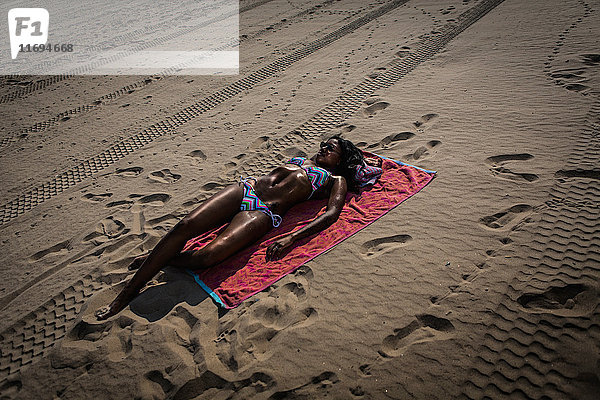 Frau beim Sonnenbad auf einem Handtuch am Strand