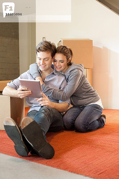 Junges Paar sitzt auf dem Boden und schaut auf ein digitales Tablett