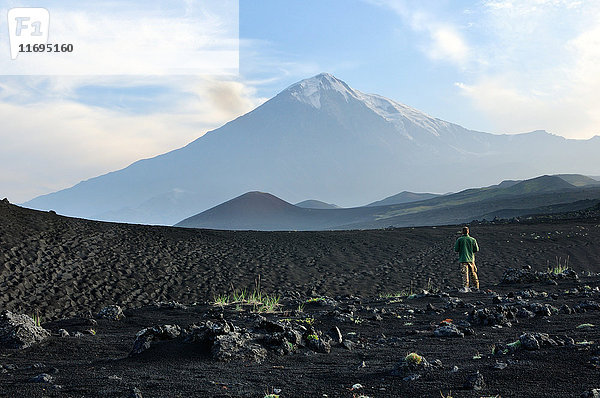 Im Lavafeld stehender Mann mit dem Vulkan Tolbachik im Hintergrund  Halbinsel Kamtschatka  Russland