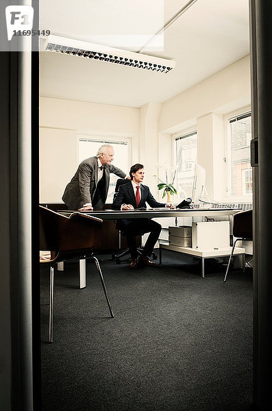 Junger Geschäftsmann am Schreibtisch mit führendem Mann im Amt