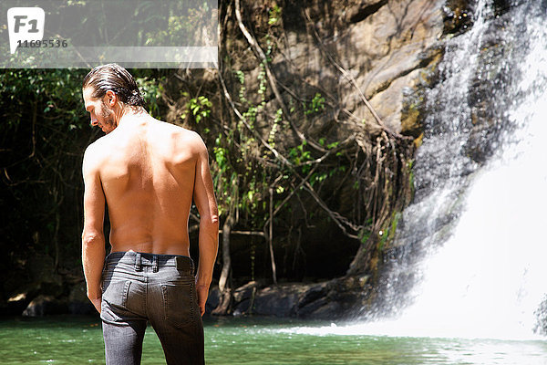 Mann mit nackter Brust am Wasserfall stehend