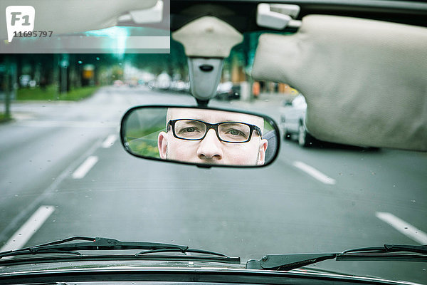 Spiegelung eines jungen Mannes mit Brille beim Autofahren im Rückspiegel