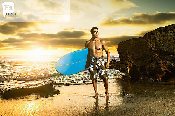 Mann trägt Surfbrett an felsigem Strand