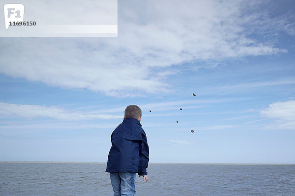 Kleiner Junge wirft Steine ins Meer