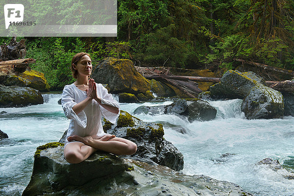 Frau meditiert auf Felsen am Wasser