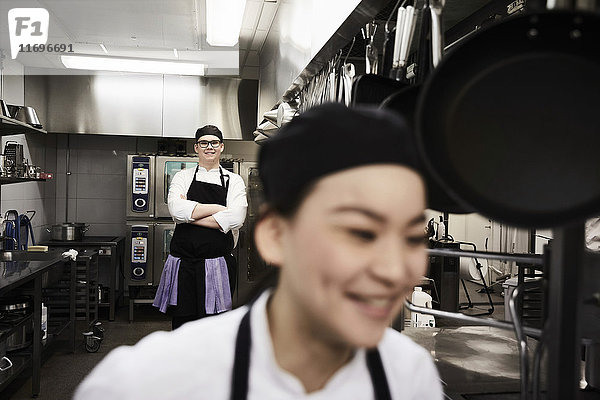 Porträt des selbstbewussten Küchenchefs mit Kollege im Vordergrund in der Großküche