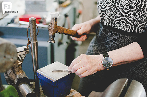Mittelteil einer älteren Frau  die auf Metall hämmert  um in der Werkstatt Schmuck herzustellen.