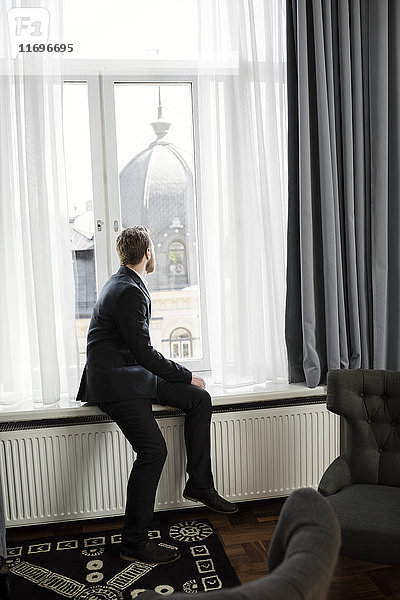 Geschäftsmann auf der Fensterbank sitzend mit Blick auf die Kuppel im Hotelzimmer