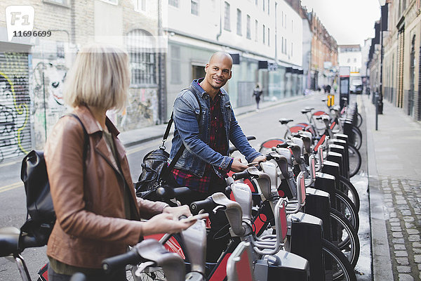 Ein multiethnisches Paar  das Fahrräder vom Fahrradstand in der Stadt leiht.