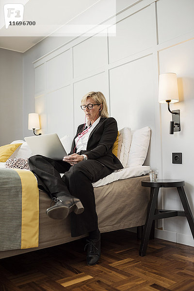 Geschäftsfrau im Bett sitzend mit Laptop an der Wand im Hotelzimmer