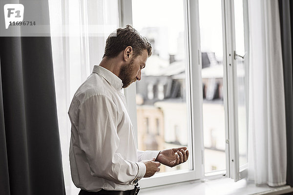 Seitenansicht des Geschäftsmannes beim Anziehen am Fenster im Hotelzimmer