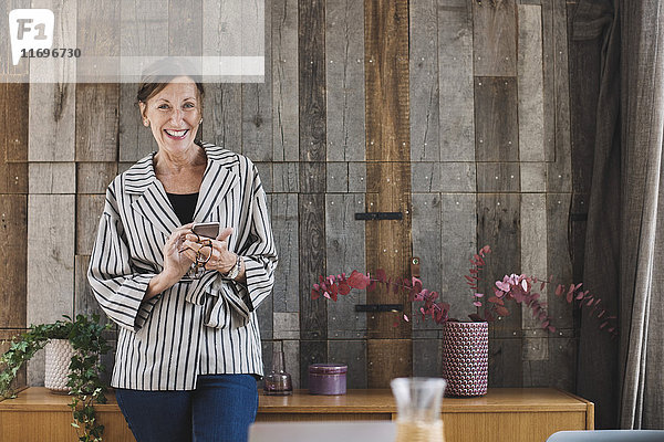 Porträt einer glücklichen Geschäftsfrau  die ein Smartphone gegen Holzverkleidung in einem tragbaren Bürowagen hält.