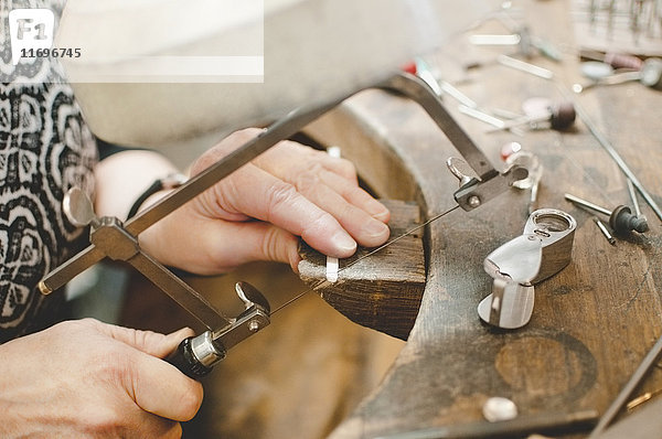 Schnittbild einer älteren Frau  die Metall mit der Handsäge in der Schmuckwerkstatt schneidet.